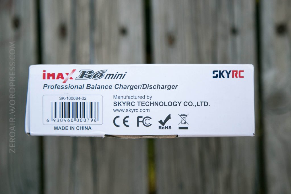 A white product box labeled iMAX B6 mini Professional Balance Charger/Discharger with SKRC logo and certification icons. Manufacturer and product details are visible. Box rests on a wooden surface.