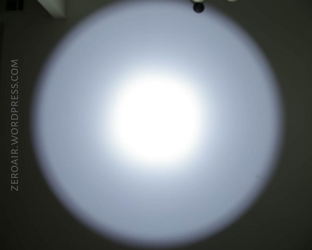 A bright white circular beam of light is projected onto a wall in a dark room. The words “ZEROAIR.WORDPRESS.COM” are faintly visible along the left edge.