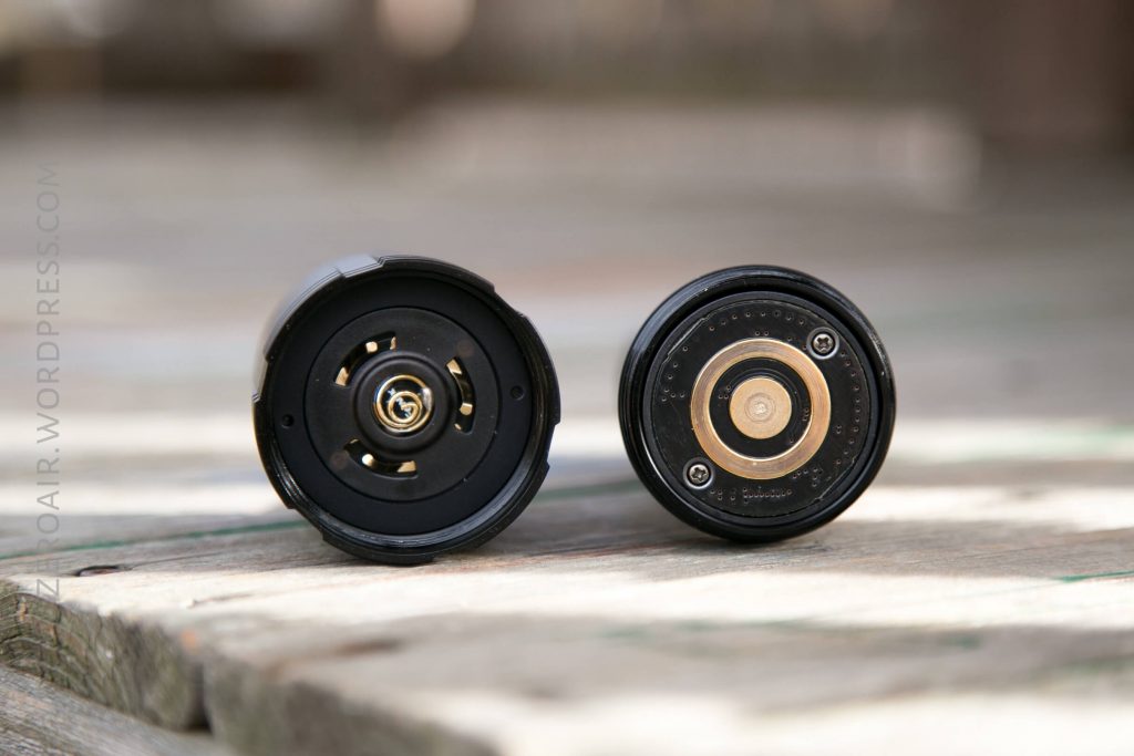 Two disassembled flashlight tail caps are placed on a wooden surface, showing their internal components, including springs and contact points, with blurred background.