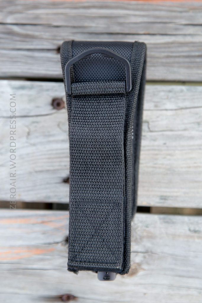 A close-up of a black, textured nylon strap with a metal rectangular loop at the top, placed on weathered wooden boards. The strap is neatly stitched and appears durable.