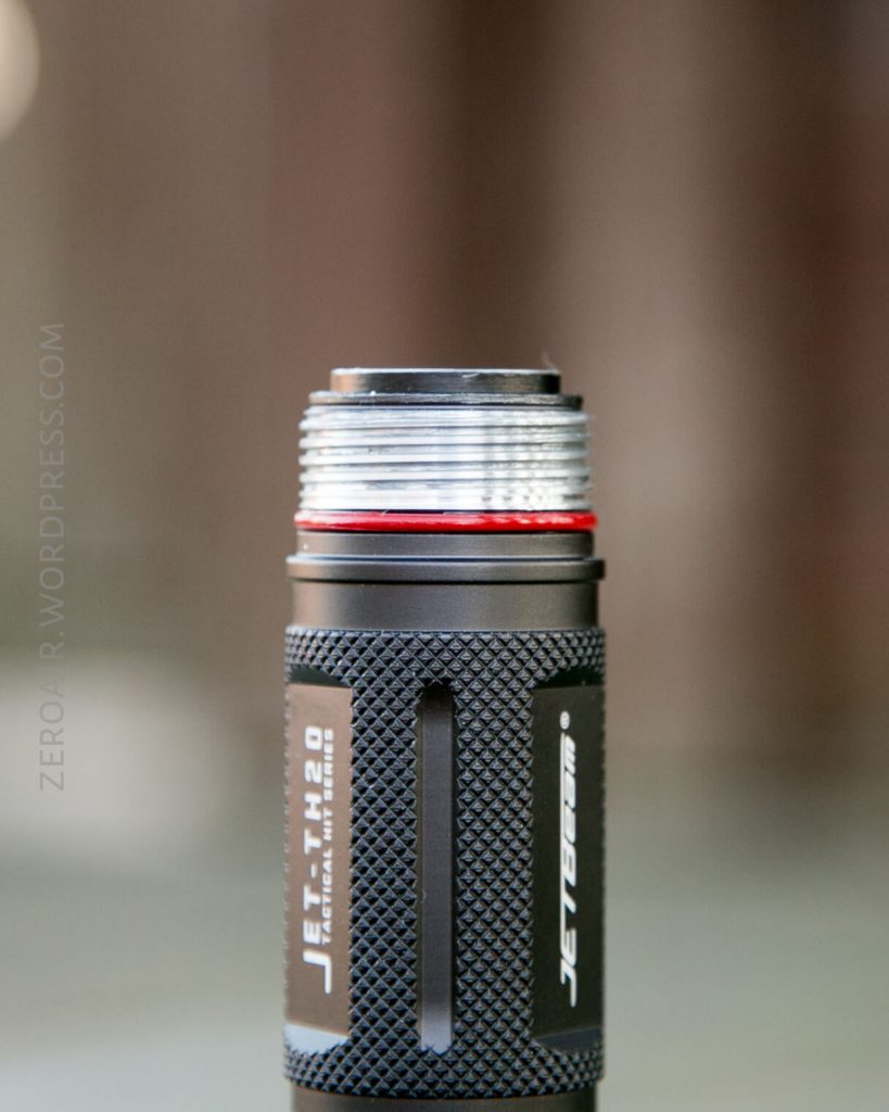 A close-up photo of the top part of a black, textured flashlight with the brand name JETBeam and model JET-1 MK 2.0 visible on the body, showing the threaded head and a red sealing ring.