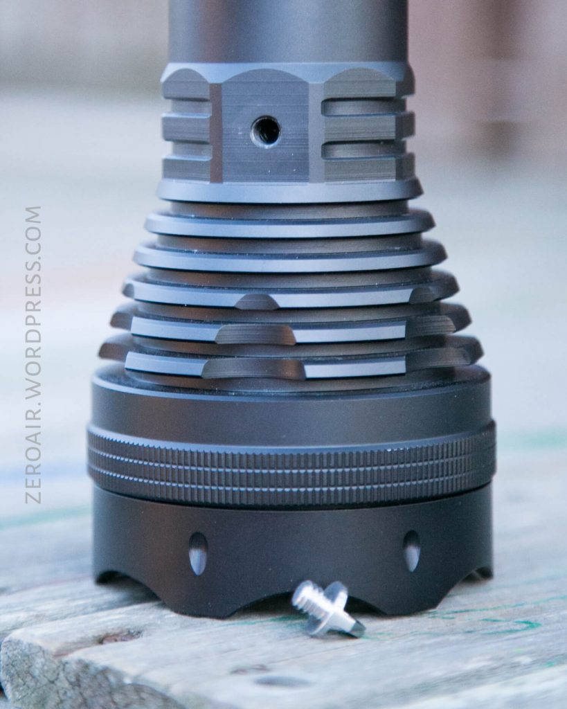A black metal flashlight with cooling fins stands upright on a wooden surface. A small silver screw rests beside its base. The text ZEROAIR.WORDPRESS.COM is visible along the left side of the image.