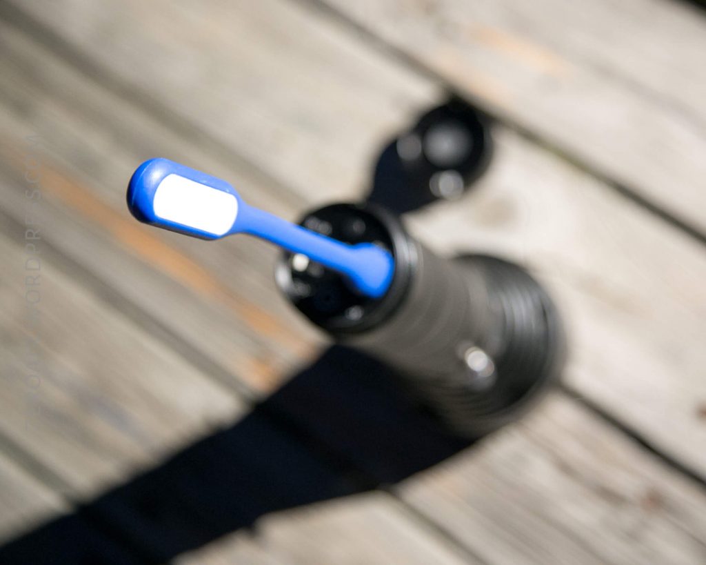 A blue and white toothbrush rests upright in a black holder on a wooden surface, with the holders cap placed nearby; the image is slightly out of focus.