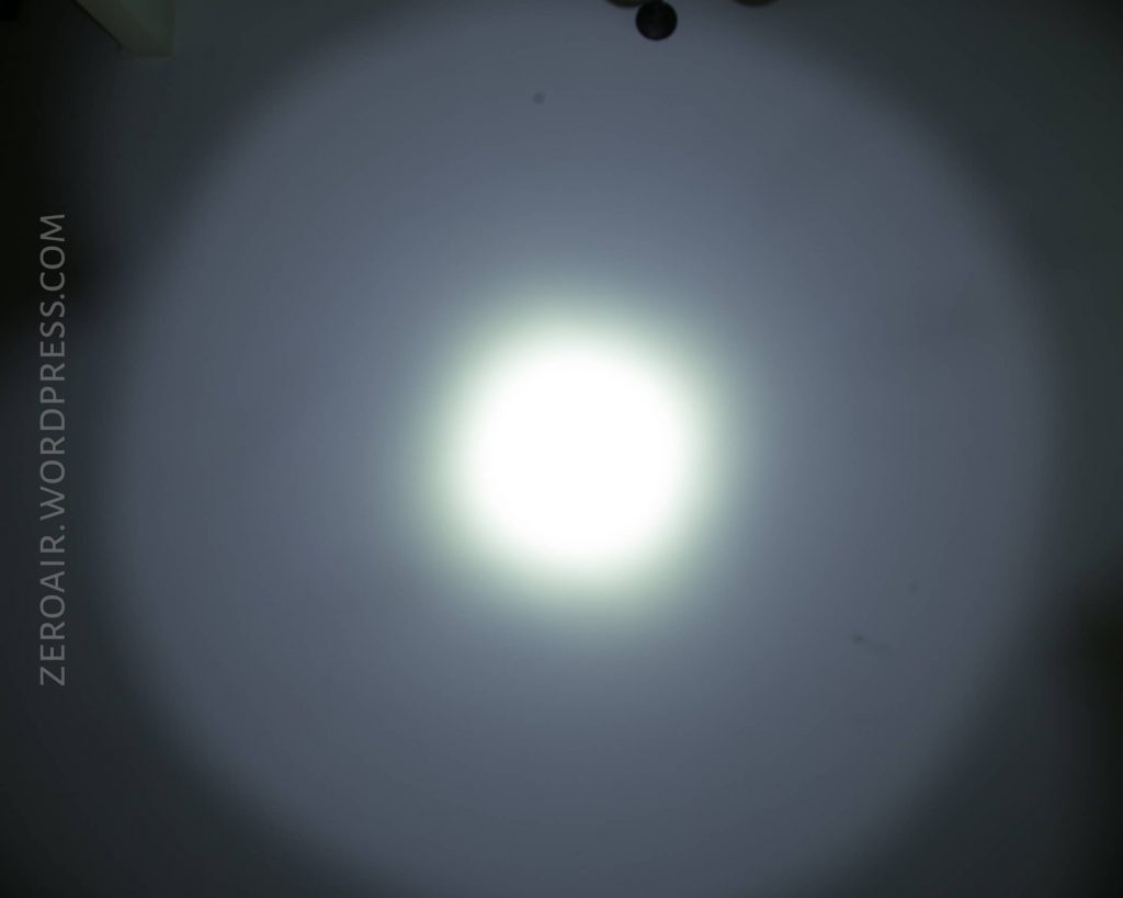 A bright white circular light is projected onto a plain surface, creating a clear central spot with a larger, dimmer halo. The background is gray. The text ZEROAIR.WORDPRESS.COM appears vertically on the left side.