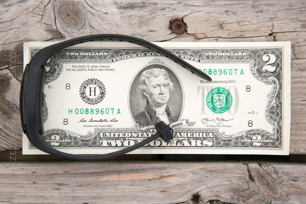 A pair of black glasses rests on top of a two-dollar bill featuring Thomas Jefferson, placed on a weathered wooden surface.