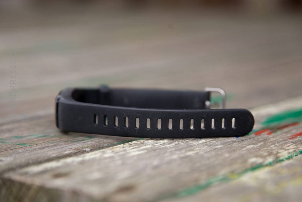 A black fitness tracker with a silicone strap resting on a weathered wooden surface, with the focus on the strap’s adjustment holes.