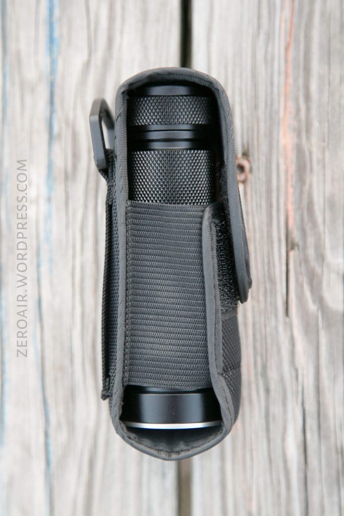 A black cylindrical object in a textured black fabric case with a Velcro flap, photographed from above on a wooden surface. The text ZEROAIR.WORDPRESS.COM appears vertically on the left side.