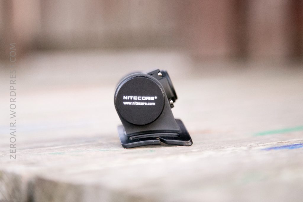 A small black clip labeled NITECORE® www.nitecore.com is placed on a wooden surface. The image is focused on the clip, with a blurred background and ZEROAIR.WORDPRESS.COM faintly visible on the left.