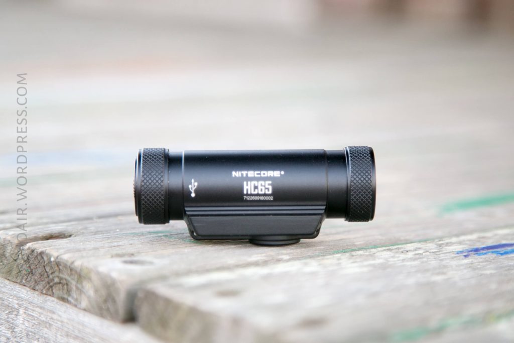 A black Nitecore HC65 flashlight rests horizontally on a weathered wooden surface, showing its brand name and model number clearly.