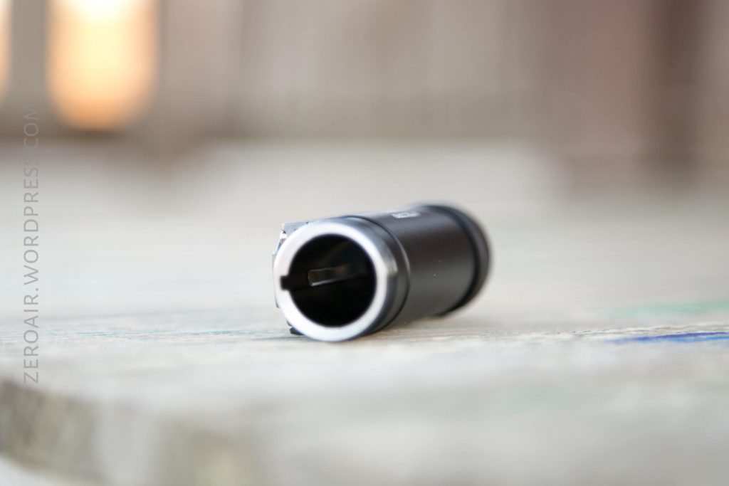 A small cylindrical black metal object lies horizontally on a flat, light-colored surface with blurred background; its interior and end are visible in the foreground. The words ZEROAIR.WORDPRESS.COM are faintly visible on the left side.
