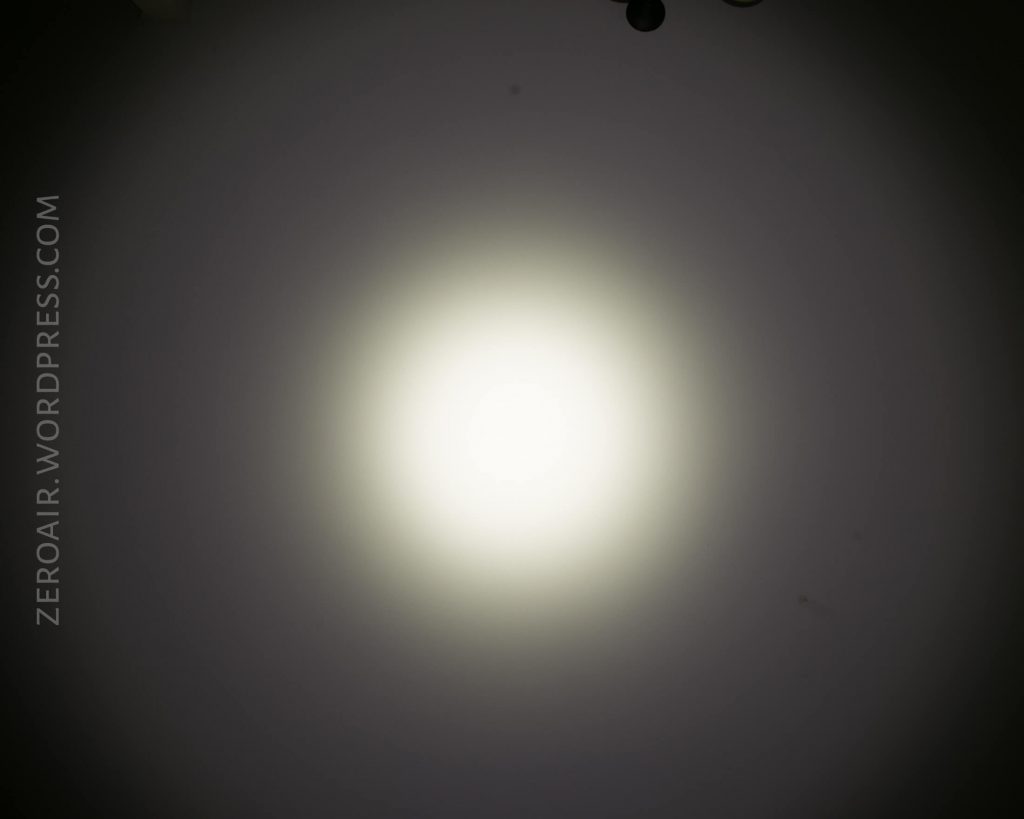 A flashlight beam creates a bright white circle of light on a plain surface with soft, darker edges. The text ZEROAIR.WORDPRESS.COM appears vertically along the left side.