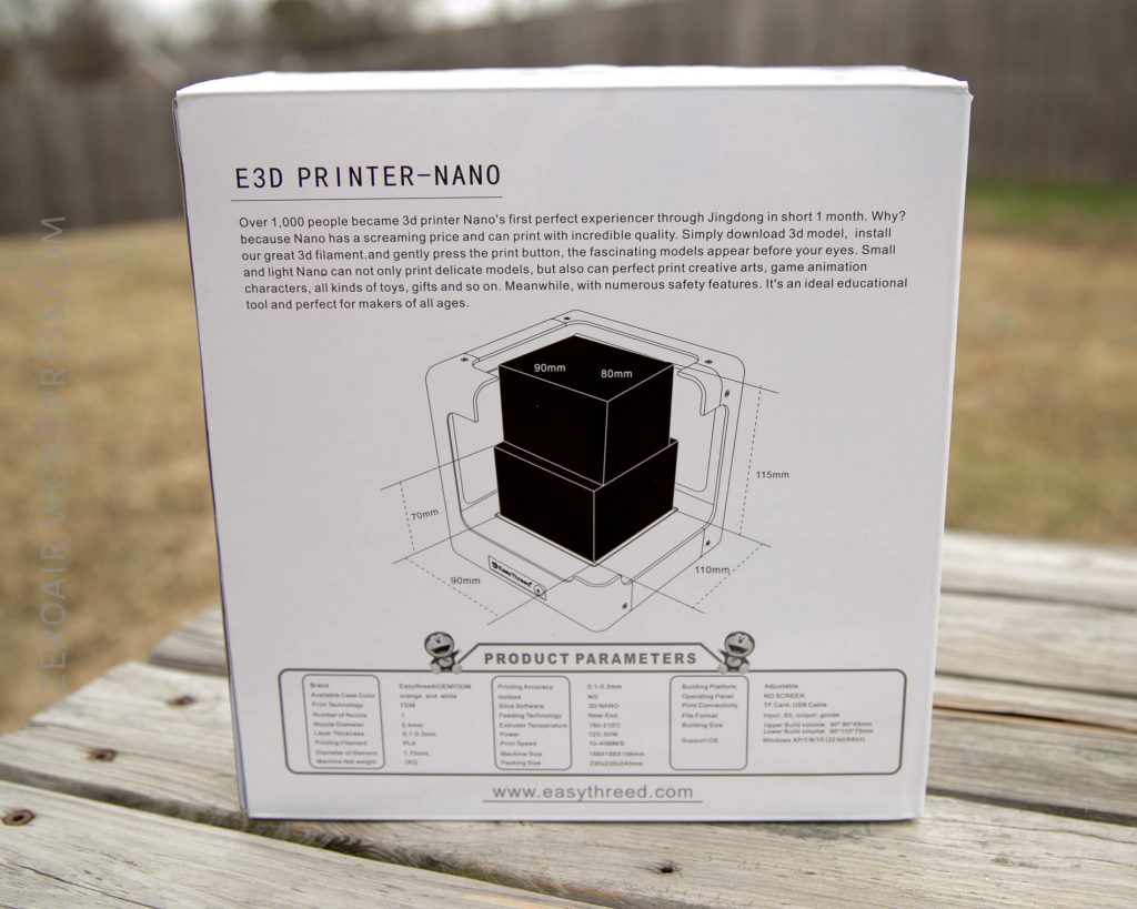 A box for the E3D Printer-Nano sits on a wooden surface outdoors. The box displays specs, a diagram of the printer’s print area, and descriptive text about the product’s features and parameters.