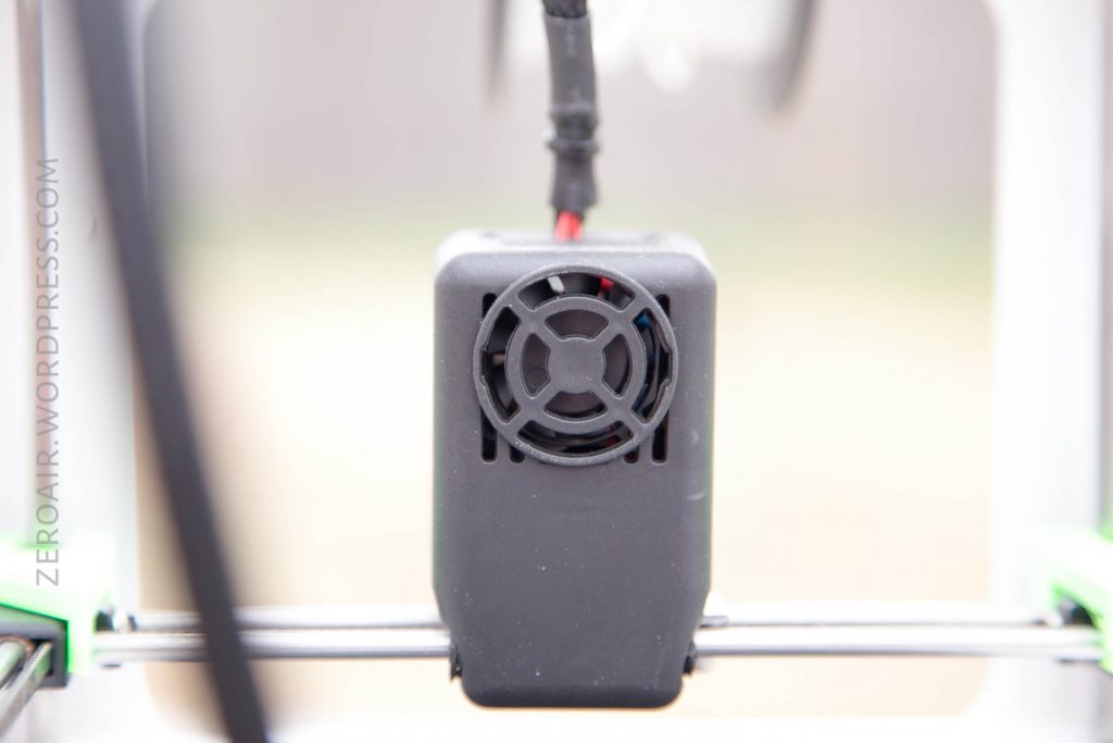 Close-up of a black plastic cooling fan housing with a circular vent on a piece of electronics, possibly 3D printer hardware. The image is slightly out of focus, with text ZEROAIR.WORDPRESS.COM on the left.