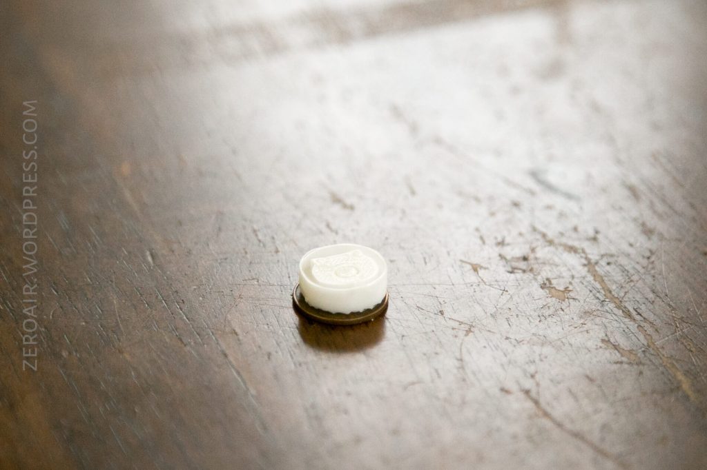 A single white round mint with a brown bottom sits on a scratched wooden surface. The background is slightly blurred. The words ZEROAIR.WORDPRESS.COM appear vertically along the left side.