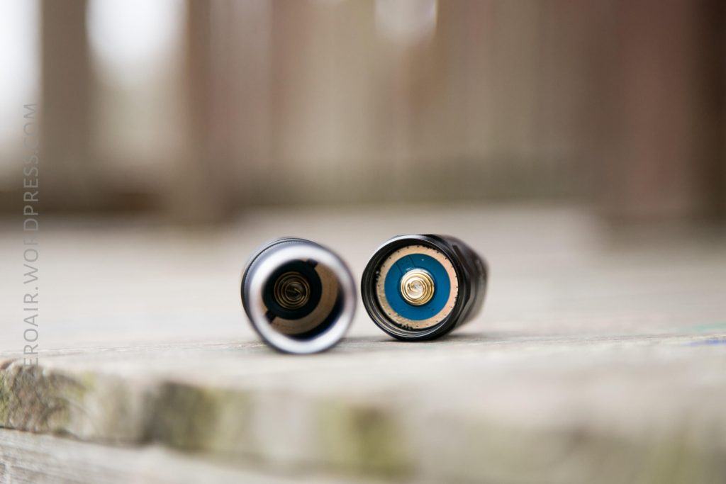 Close-up view of two cylindrical objects placed side by side on a wooden surface, showing the internal ends with visible metal contacts and a blue ring on one of them.