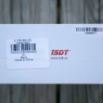 A white box with barcode stickers and product information, including the words Black, Made in China, and ISDT branding, placed on a wooden surface.
