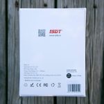 The back of an ISDT C4 product box displays technical specifications, certifications, a QR code, website URL, and manufacturing information against a wooden background.