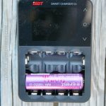 A single Efest IMR 18650 battery is placed in the bottom slot of an ISDT Smart Charger C4, which is positioned on a wooden surface. The chargers screen is off.