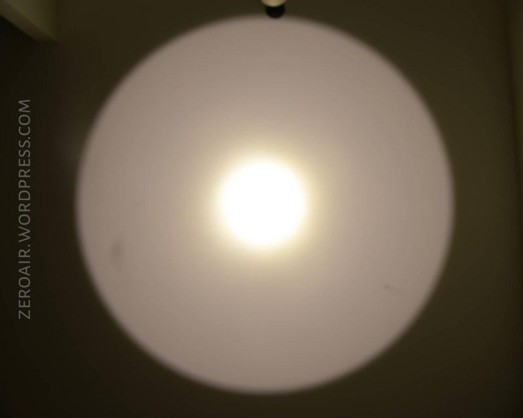 A bright white circular light beam is projected onto a wall in a dark room. The photo has the watermark ZEROAIR.WORDPRESS.COM on the left side.