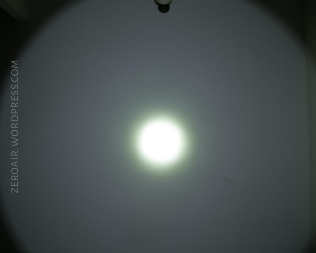 A bright white circular spotlight is cast on a gray wall in a dark room, with the text ZEROAIR.WORDPRESS.COM vertically along the left side. The edge of a ceiling or wall is visible in the upper right corner.