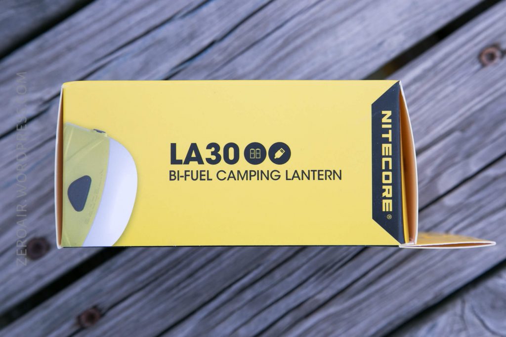 A yellow box labeled LA30 Bi-Fuel Camping Lantern with the brand name Nitecore on the side, placed on a wooden surface. The box features simple black text and icons.