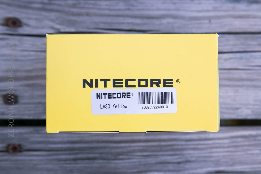 A yellow box with the text NITECORE printed in black. Below it, a white barcode sticker reads LA30 Yellow with a barcode and numbers. The box is on a wooden surface.