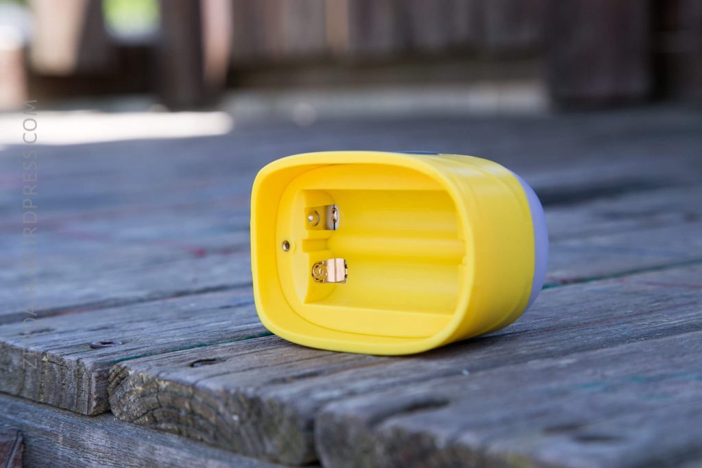 A yellow flashlight shown lying on its side on a wooden surface, exposing the open battery compartment without any batteries inside.
