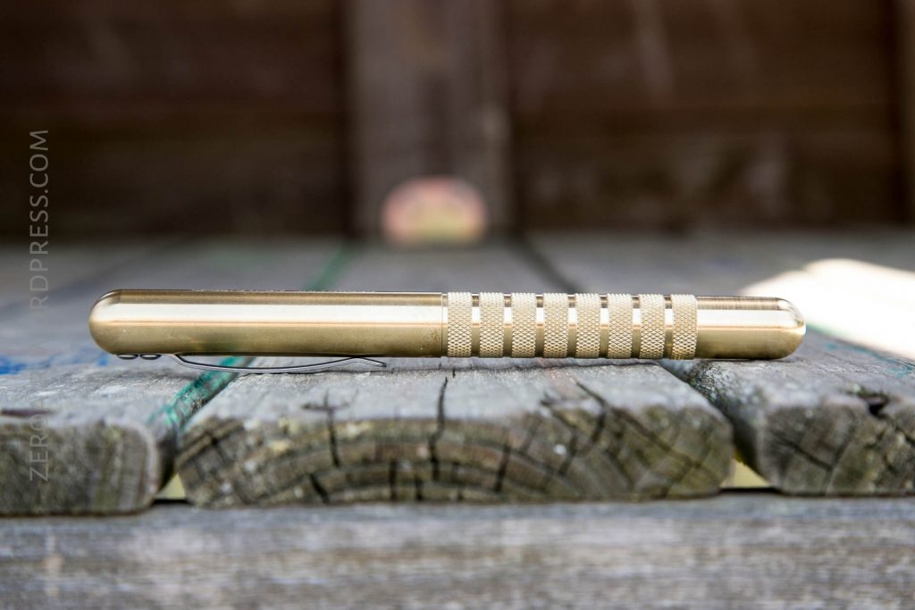 A metallic pen with a textured grip lies horizontally on a weathered wooden surface, with a blurred brown background.