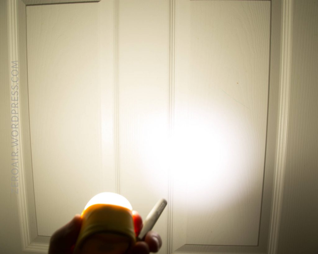 A hand holding a small flashlight is shining a bright beam of light onto a white, paneled door. The words ZEROAIR.WORDPRESS.COM are faintly visible vertically on the left side.