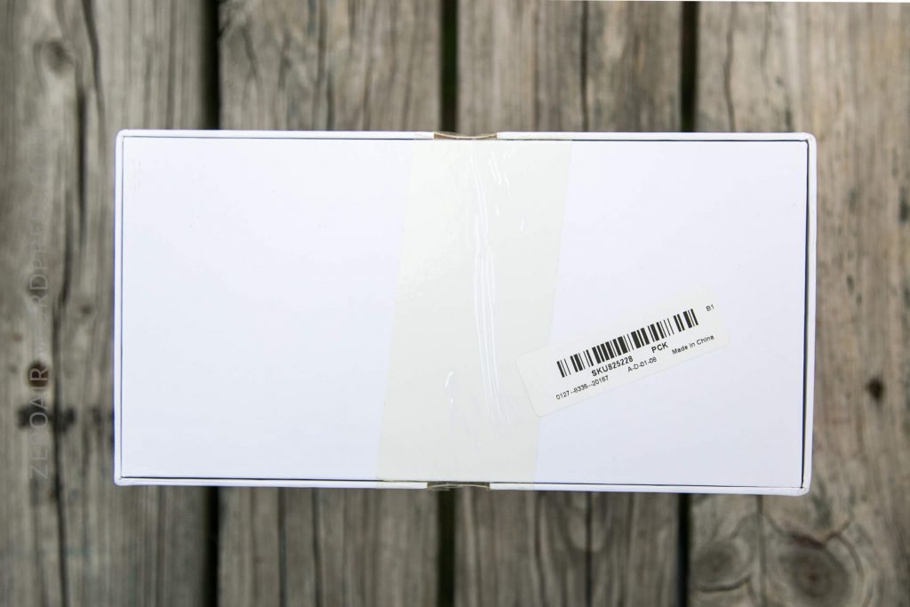 A rectangular white box with a barcode sticker and a strip of clear tape sealing the center, placed on a weathered wooden surface.