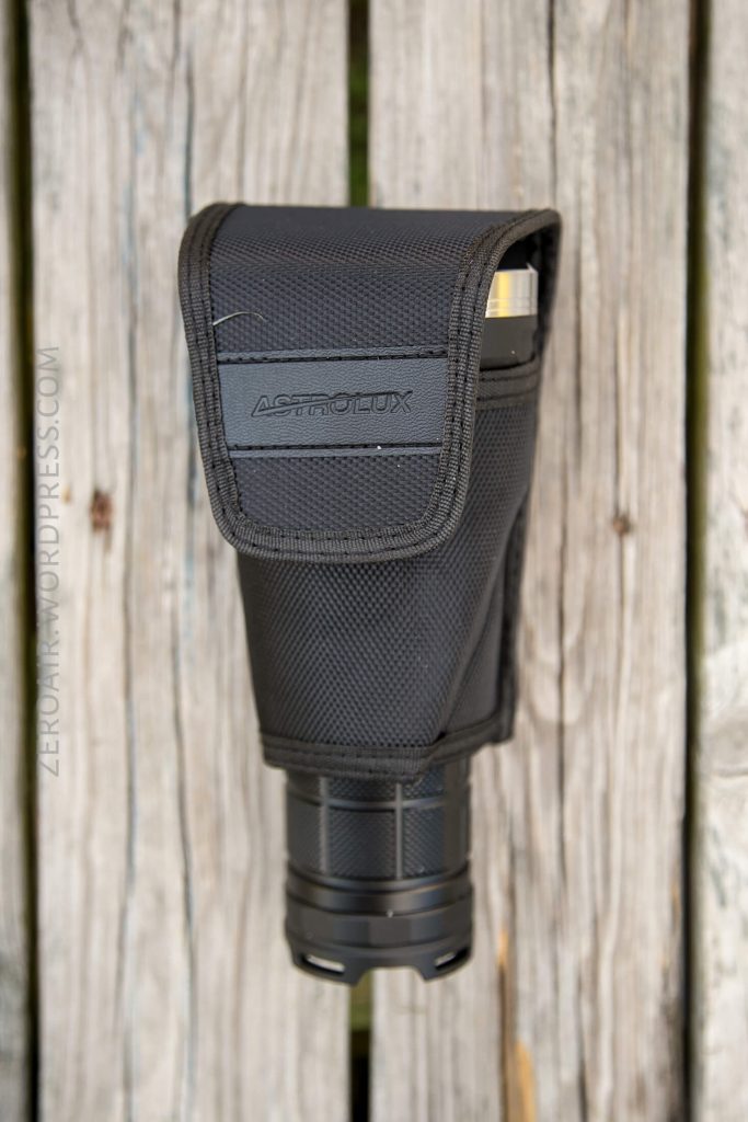 A black nylon flashlight holster with a flap labeled ASTROLUX holds a flashlight. The holster is placed on a weathered wooden surface.