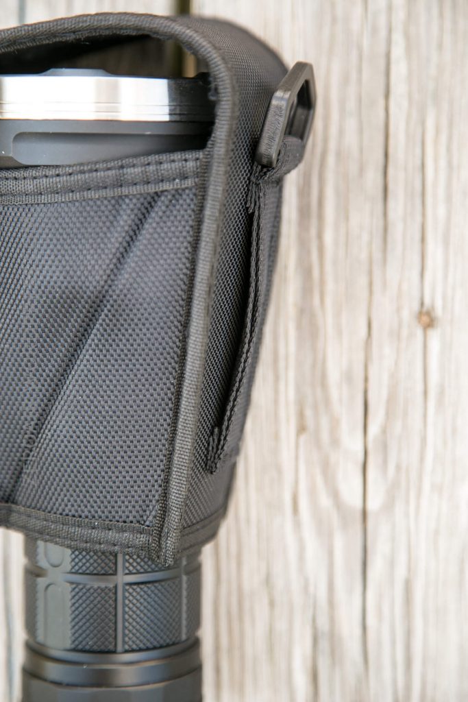 A close-up of a black textured carrying case holding a cylindrical object with a metallic rim on top, set against a background of weathered wooden planks.
