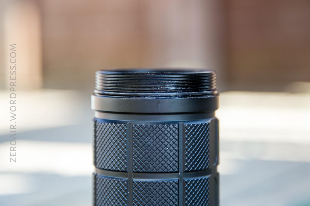 A close-up view of the top portion of a black, textured cylindrical object with threading visible at the top. The background is out of focus, and ZEROAIR.WORDPRESS.COM is written vertically on the left side.
