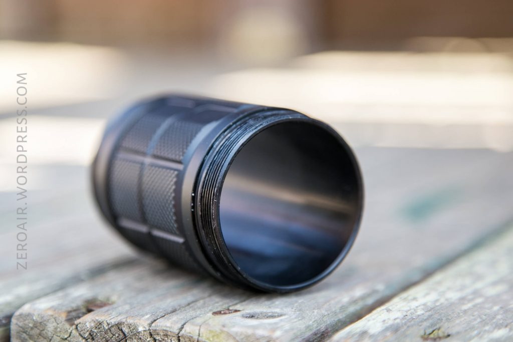 A close-up of a black, cylindrical flashlight body without its lens or end, lying on its side on a wooden surface. The image is shallow-focused, and text ZEROAIR.WORDPRESS.COM appears vertically on the left.