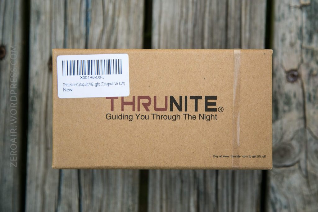A brown cardboard box with a white barcode label and the text THRUNITE Guiding You Through The Night printed on it, placed on a wooden surface.