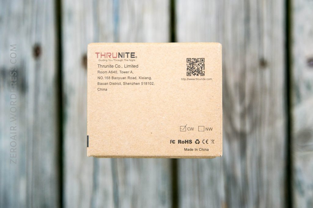 A cardboard box from ThruNite Co., Limited showing the company’s address in Shenzhen, China, product certifications, and a QR code, placed on a wooden surface.