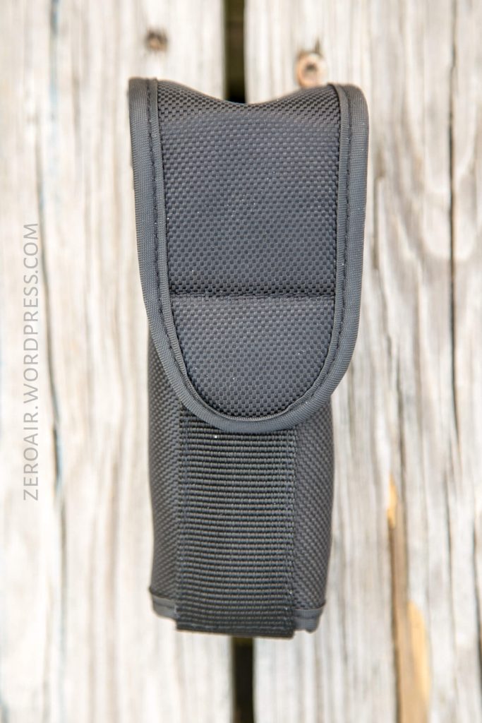 A black nylon pouch with a flap closure, photographed vertically on a weathered wooden surface. The texture of the fabric and stitching details are clearly visible. ZEROAIR.WORDPRESS.COM is written along the left side.