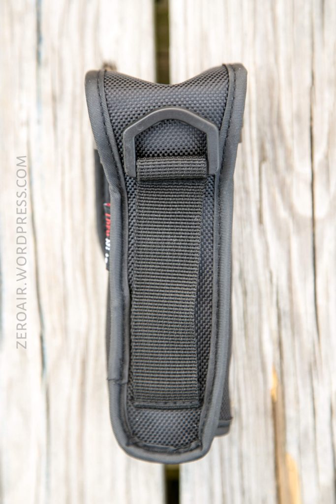 A close-up side view of a black nylon pouch with a vertical strap and plastic loop, placed on a weathered wooden surface. The text ZEROAIR.WORDPRESS.COM is visible along the left side.