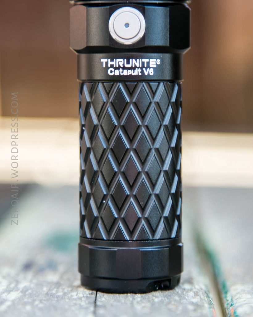 A close-up photo of the handle of a ThruNite Catapult V6 flashlight, featuring a textured diamond-patterned grip and a visible power button near the top.