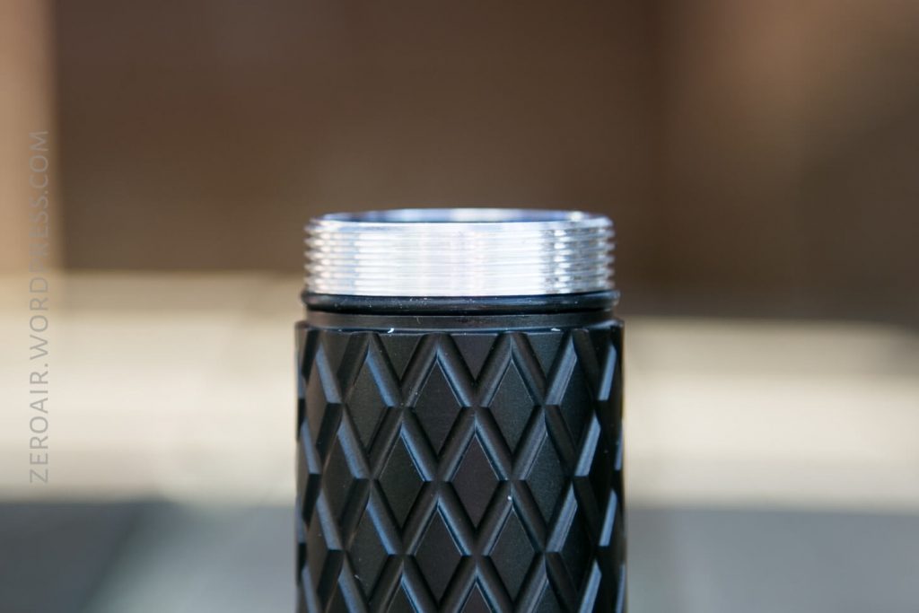 A close-up of the threaded top section of a black, textured cylindrical object, possibly a flashlight body, with a diamond pattern and a blurred background. The words ZEROAIR.WORDPRESS.COM are visible along the left side.