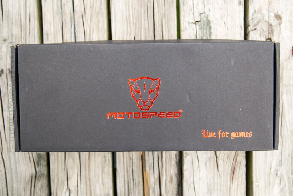 A rectangular black box with the red Motospeed logo and the text MOTOSPEED and Live for games printed on the lid, placed on a weathered wooden surface.