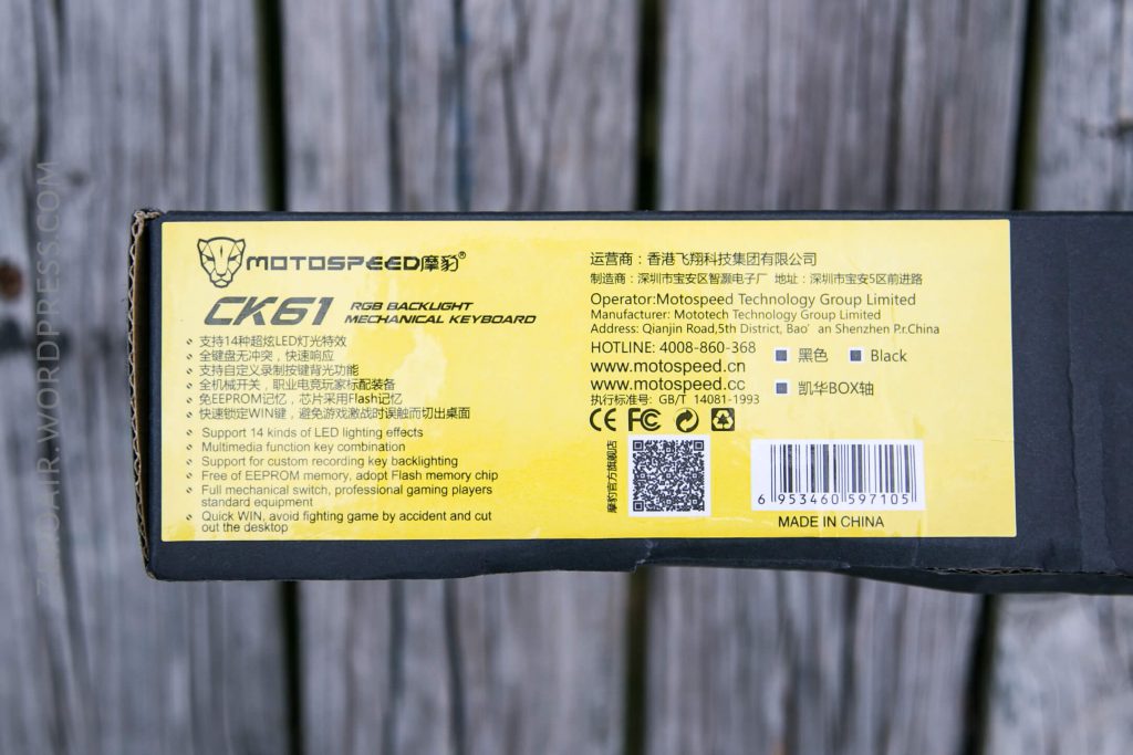 A close-up of a box for the Motospeed CK61 RGB Backlight Mechanical Keyboard showing product specifications, company information, and a barcode against a wooden background.