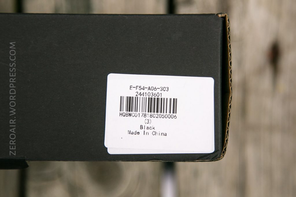 A close-up of a black box with a white label showing a barcode, product code, number 33, color Black, and Made in China. The background is a wooden surface. ZEROAIR.WORDPRESS.COM is faintly visible on the left.