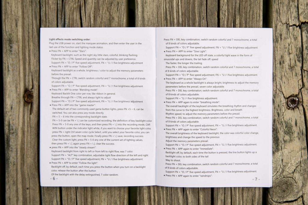An open instruction manual with text detailing keyboard light effects and function key shortcuts, resting on a wooden surface with visible planks. Pages are numbered 6 and 7.