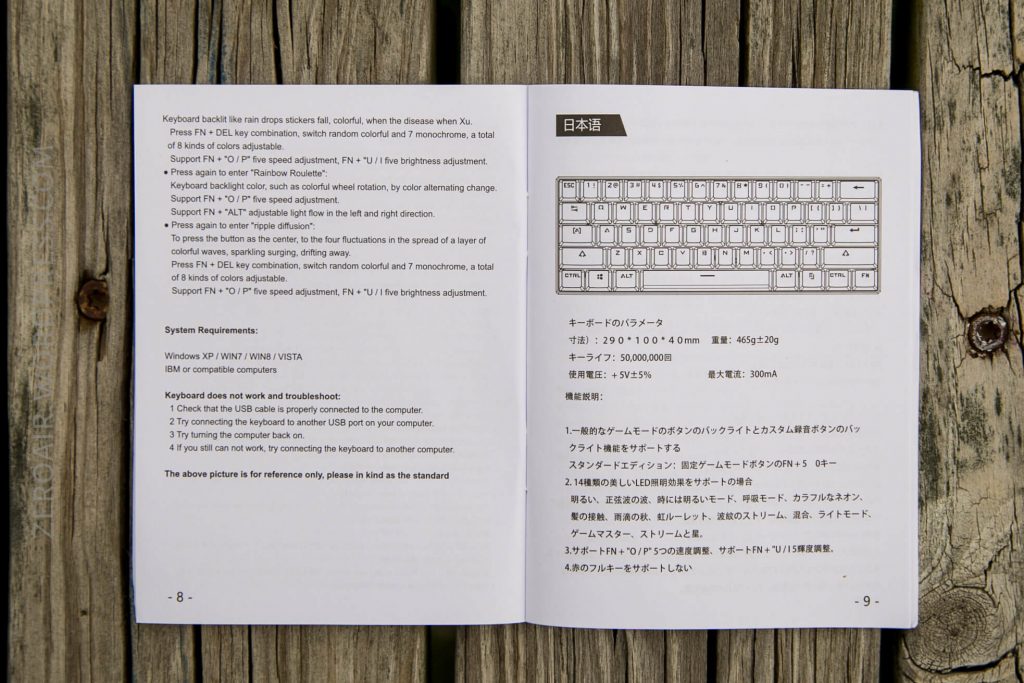 An open manual on a wooden surface shows English instructions and a diagram of a keyboard on the left page, with Japanese text and another keyboard illustration on the right page.