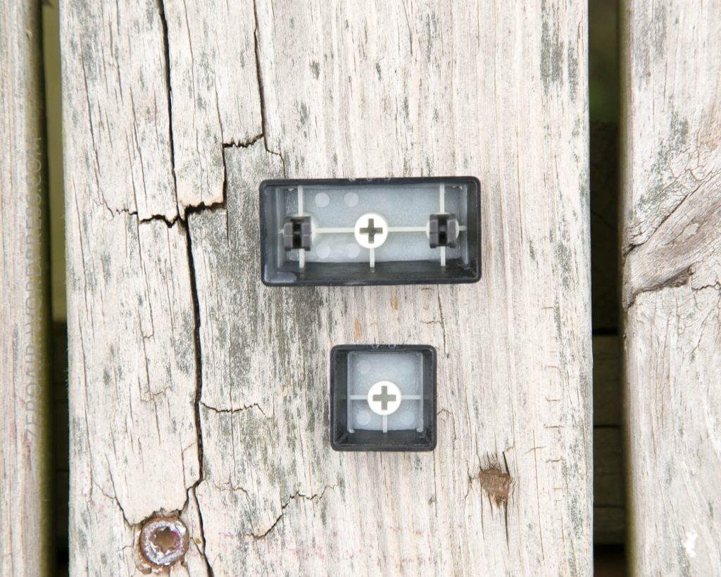 A close-up of two rectangular plastic electrical connectors mounted on weathered, cracked wooden planks. The connectors have visible metal contacts inside and are secured with cross-shaped fasteners.
