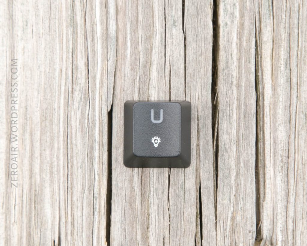 A single black keyboard key with a white U and a light bulb icon sits on weathered wooden planks. The words ZEROAIR.WORDPRESS.COM appear vertically along the left side.