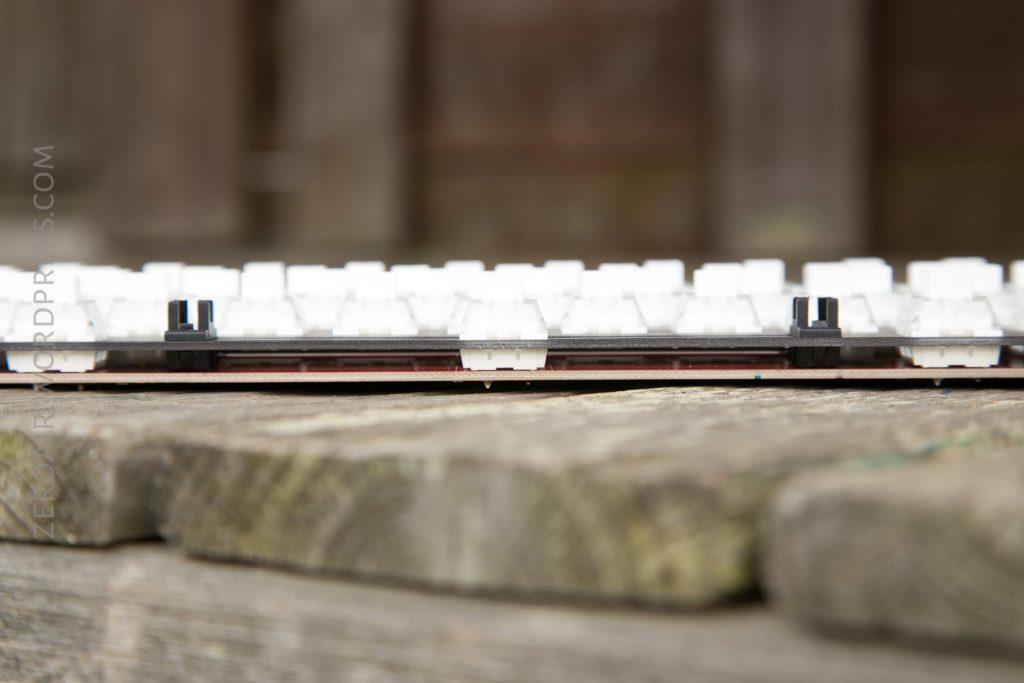 A close-up side view of a mechanical keyboard without keycaps, placed on a weathered wooden surface, with the switches and circuit board visible.