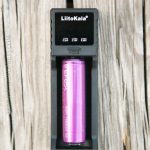 A single purple Efest IMR 18650 battery is placed inside a black LiitoKala battery charger, which rests on a weathered wooden surface.