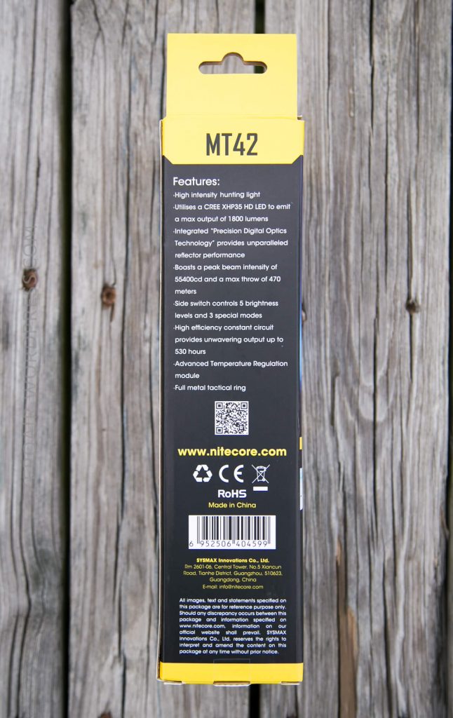 A close-up of the side panel of a NITECORE MT42 flashlight box, listing features and specifications in yellow and white text on a black background, placed on a weathered wooden surface.